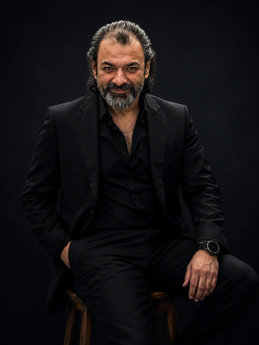 Muhammad Usman A. Khan, standing with arms crossed in a dark suit